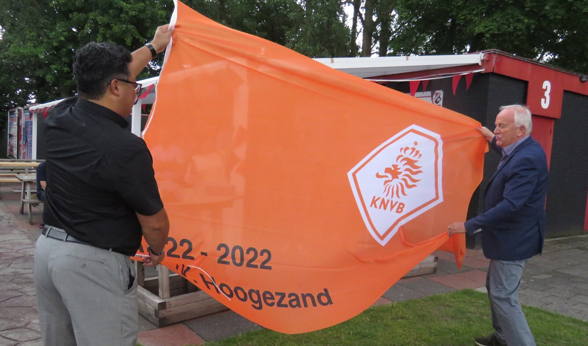 Voorzitter Andy Kasto van VV Hoogezand en David Woortman van de KNVB tonen de jubileumvlag.