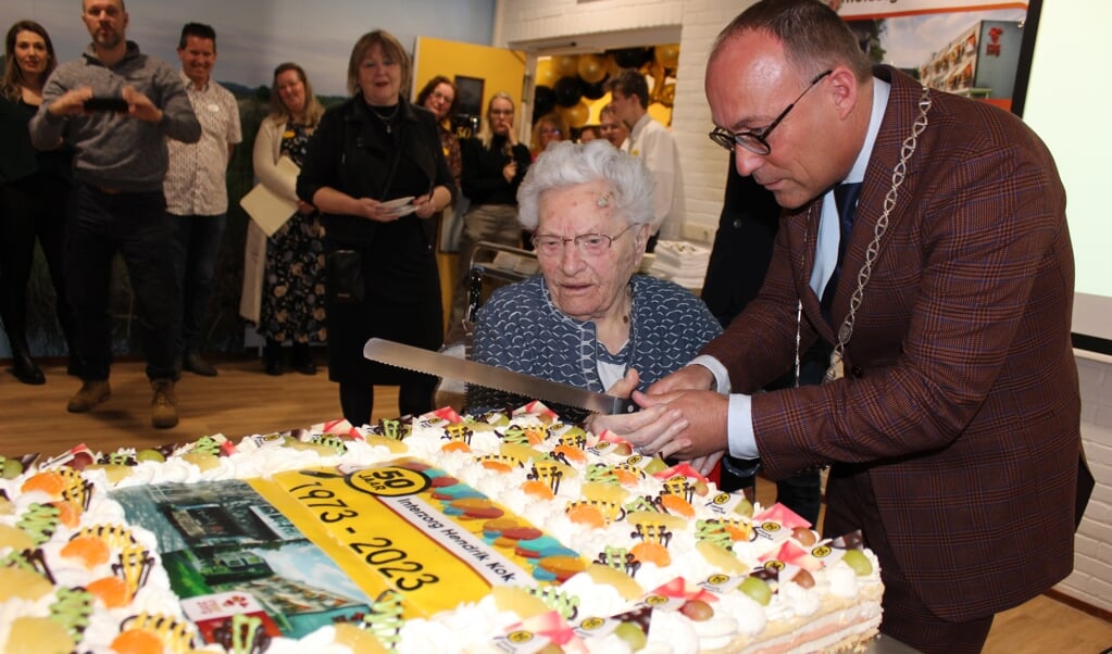 Enna van der Horn en burgemeester Hiemstra snijden de taart aan ter ere van 50 jaar Hendrik Kok. (Foto: Henry Koops) 