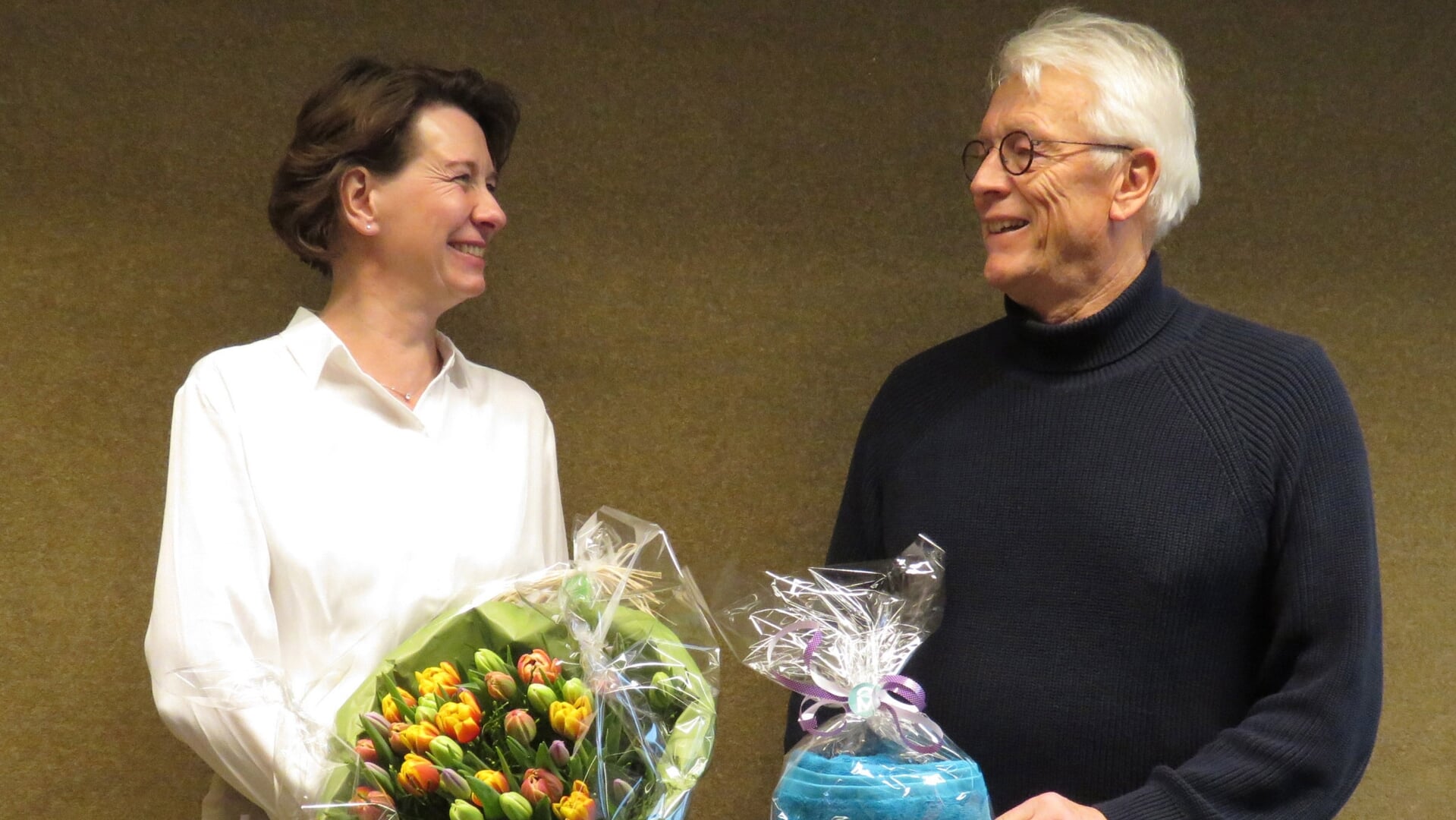 Henk Slomp ontvangt een grote bos tulpen en badhanddoek met logo van wethouders Annemiek Hoesen als waardering van het gemeentebestuur.