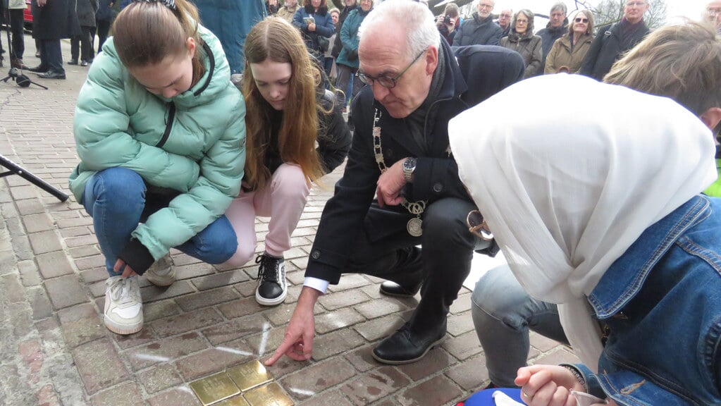 Burgemeester Hoogendoorn bekijkt met de kinderen de namen op de herdenkingstenen.