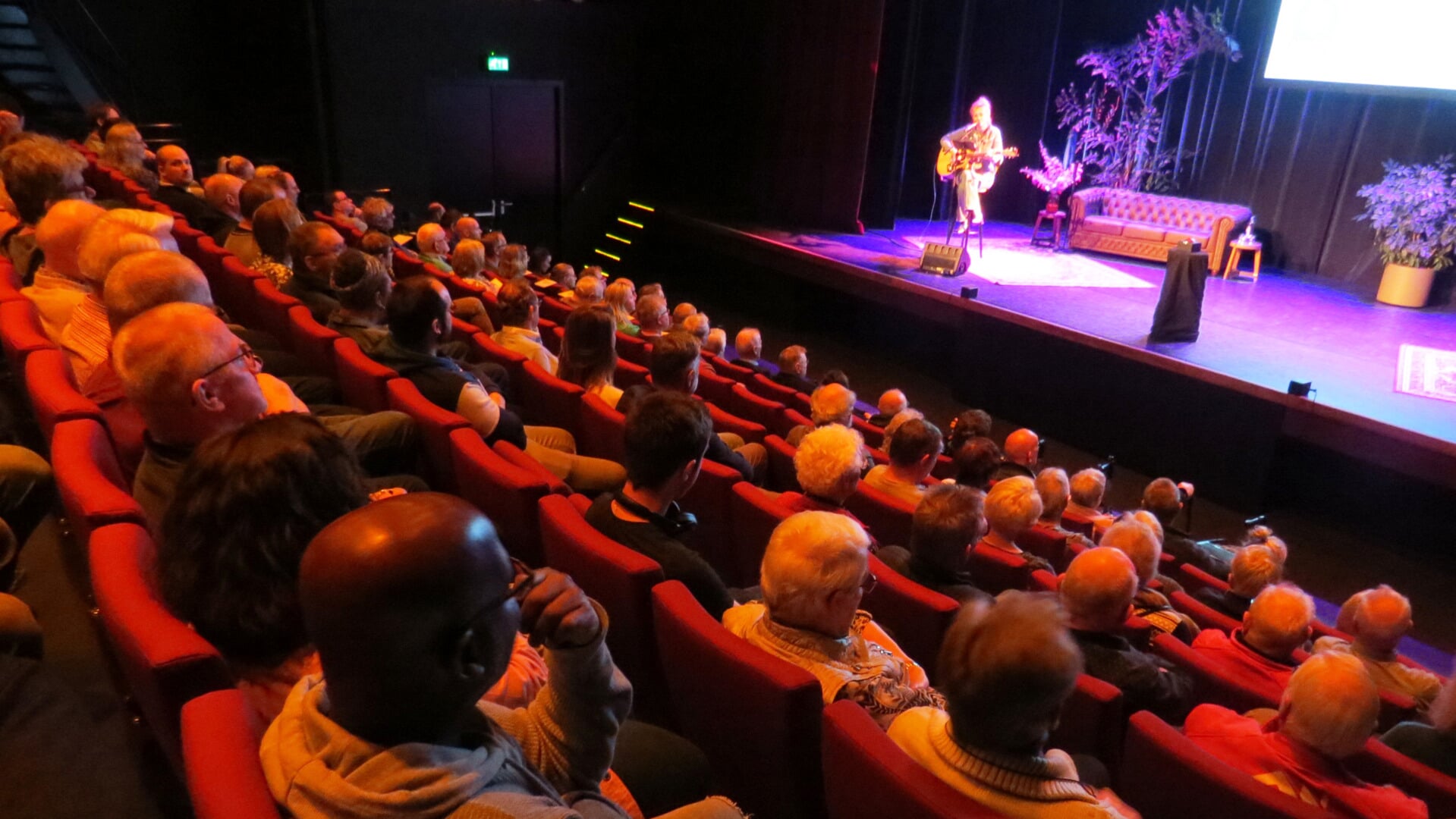 De bezoekers in de redelijk gevulde zaal luisteren naar informatie over het warmtenet en naar zangeres Jetta Post.