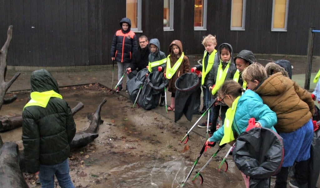 Kinderen van De Klimboom ruimen in de stromende regen samen met wethouder Ralph Lafleur het zwerfvuil rond de school op