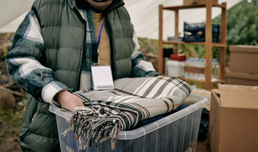 Close-up of female volunteer with badge packing stuff into container while preparing warm blanket for refugees