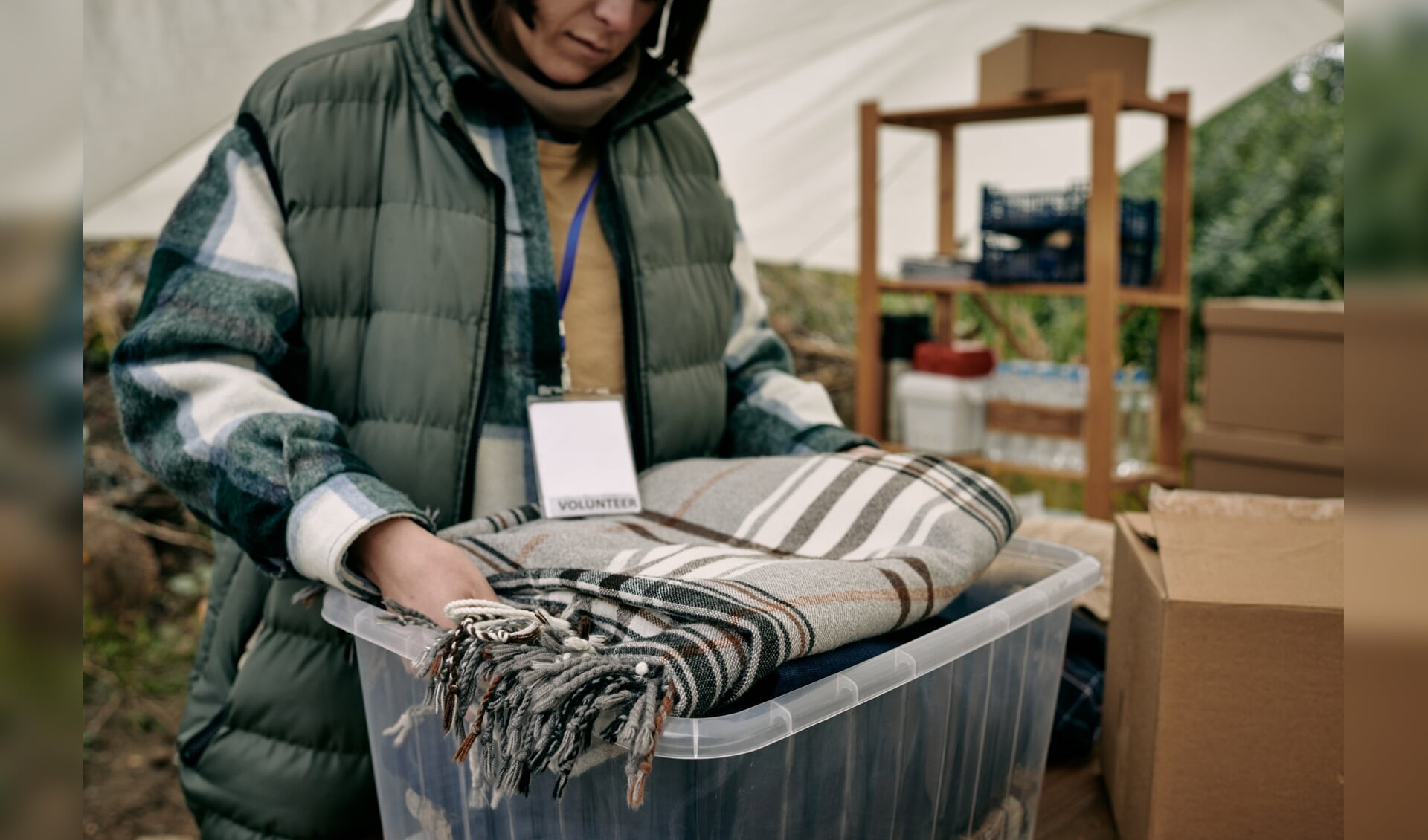 Close-up of female volunteer with badge packing stuff into container while preparing warm blanket for refugees
