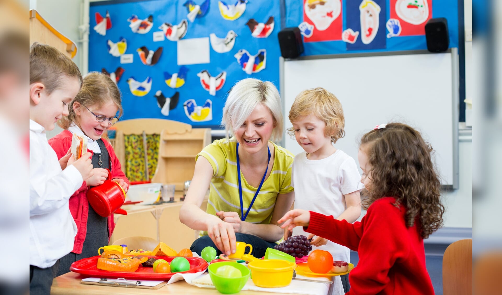 Nursery teacher playing kitchen roleplay with her students in the classroom.