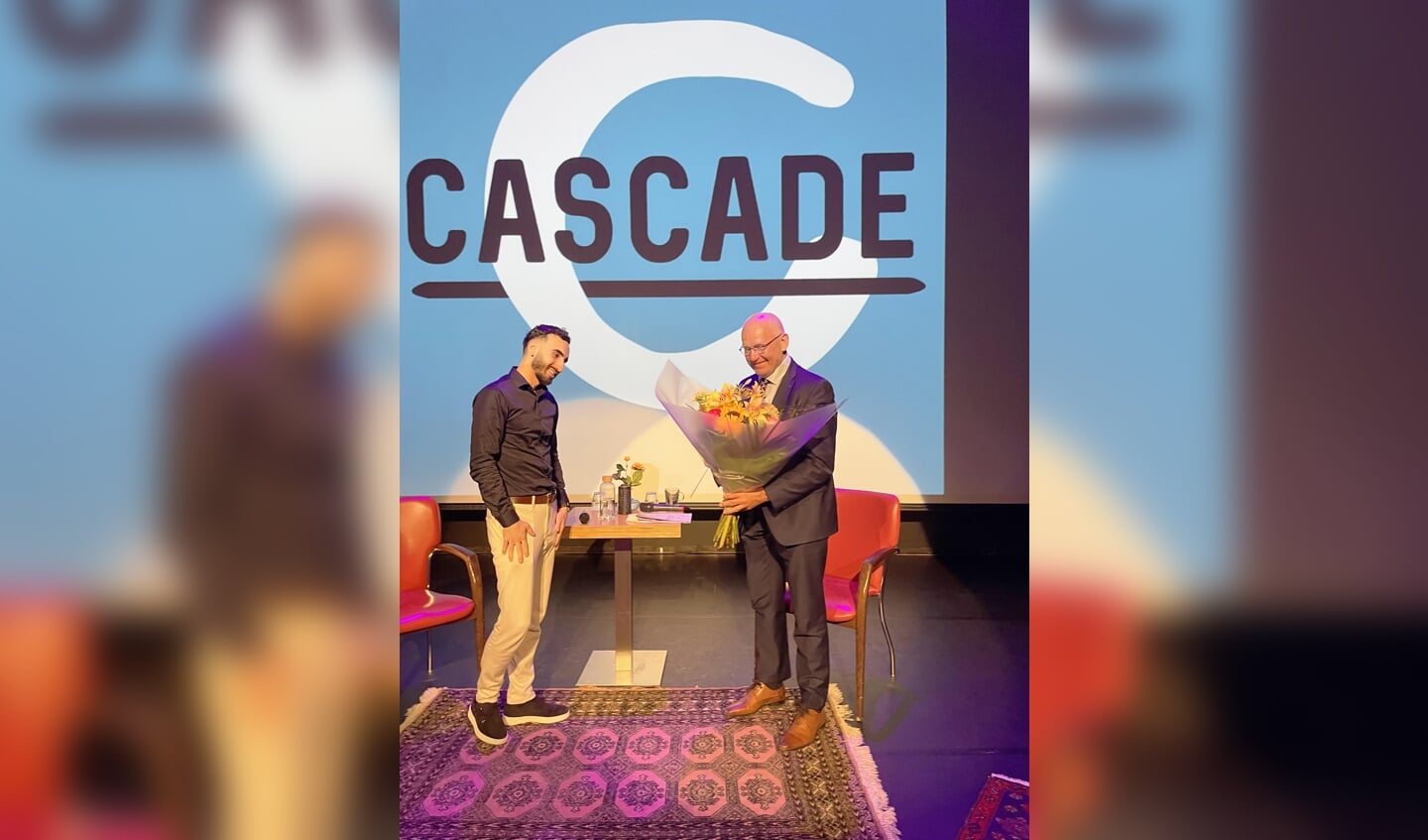 Presentator Alihan Uzun overhandigt burgemeester Heijkoop een bos bloemen als dank voor zijn medewerking.