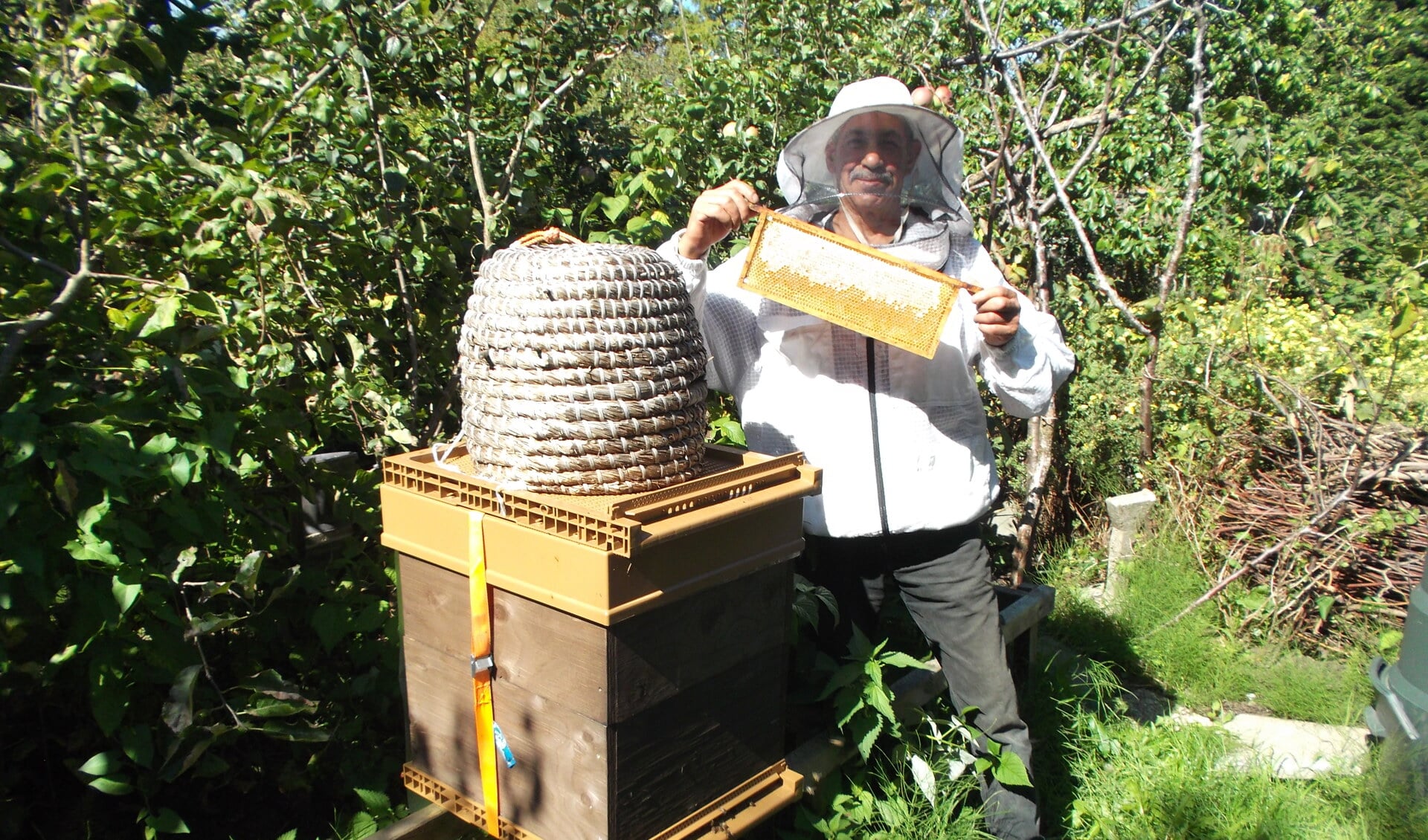 Hobby imker Aziz toont trots een gevulde honingraat bij een van zijn bijenkasten