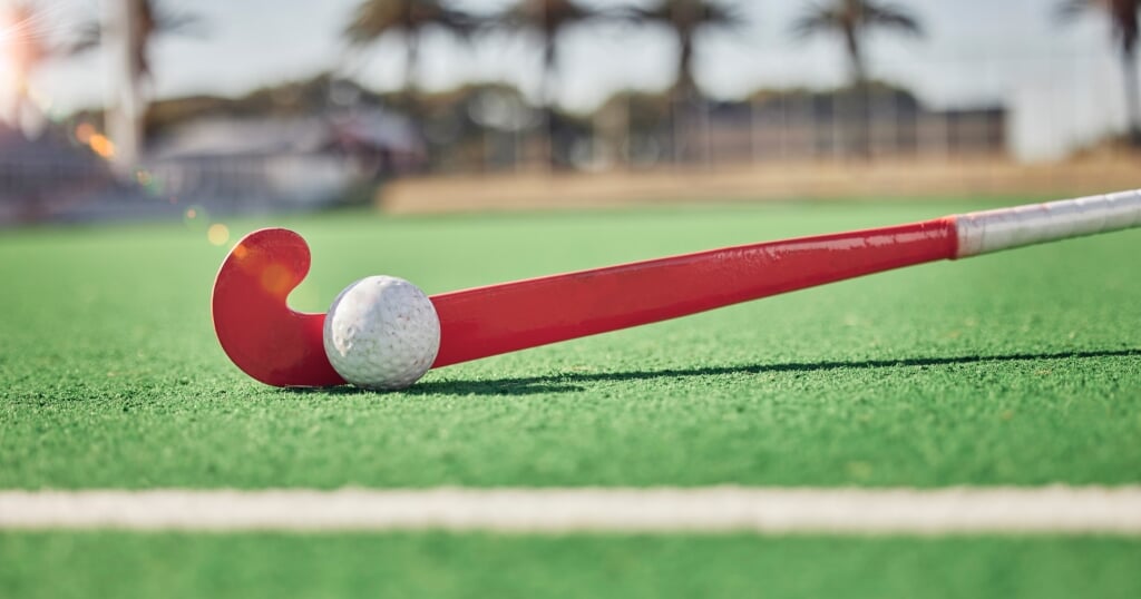 Closeup, hockey and hockey stick with ball on field in sunshine for sport, contest or competition i.