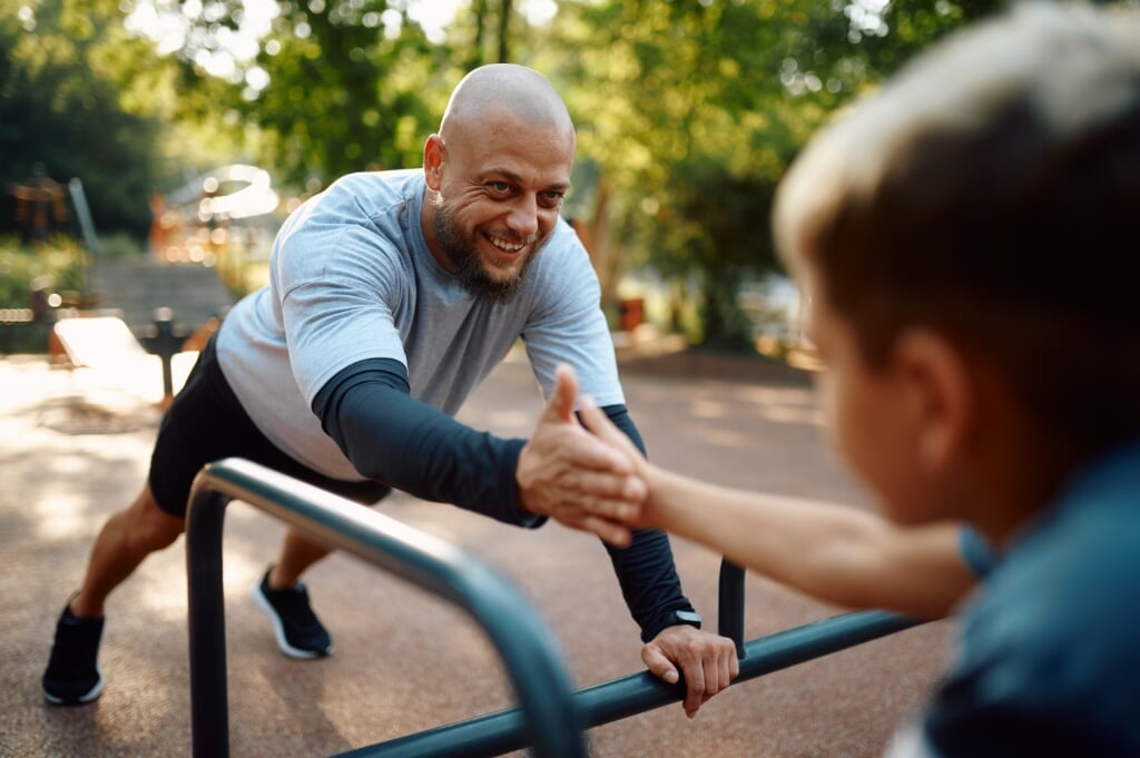 Cheerful father and son, sport training on playground outdoors. The family leads a healthy lifestyle, fitness workout in summer park
