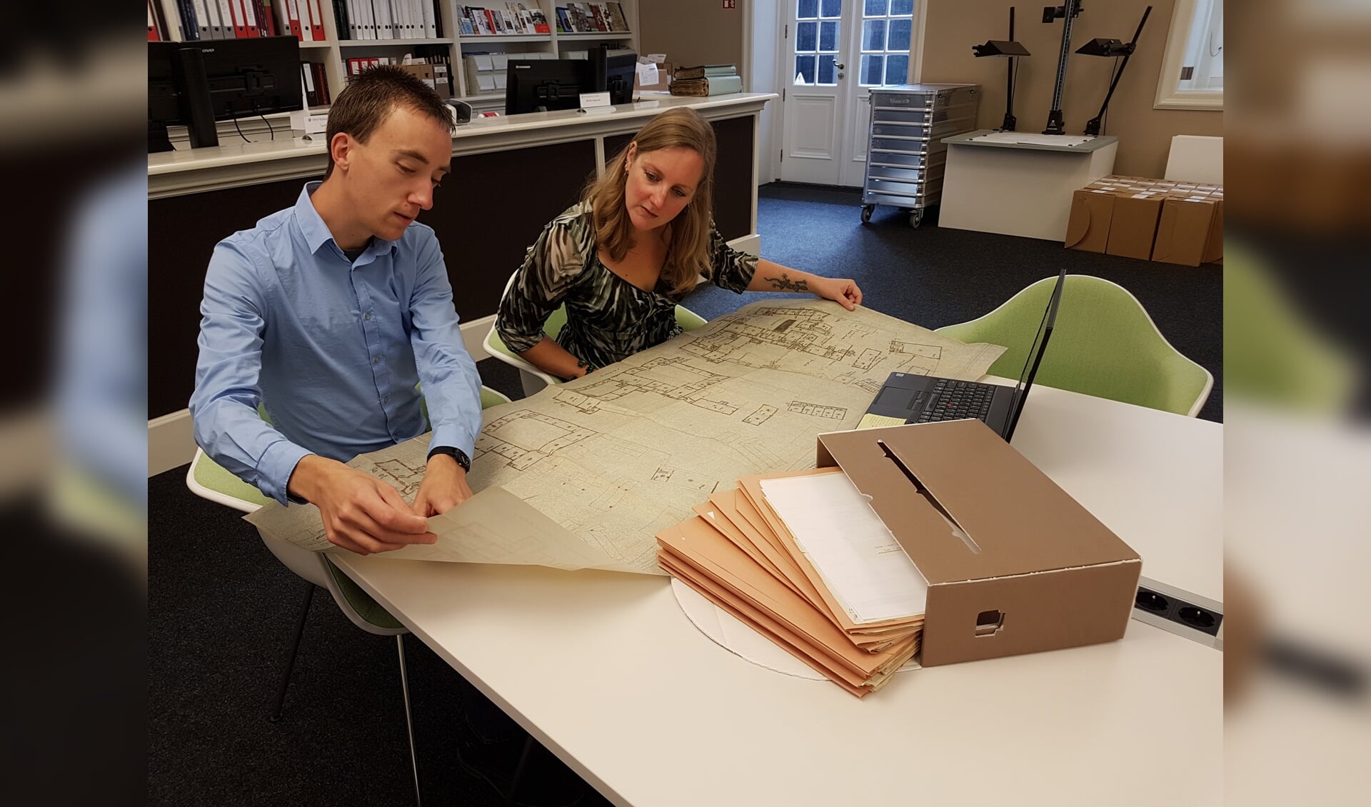 Archieffoto: Onderzoeker Bart van Eekelen toont medewerker Dienstverlening Saskia van Bavel een plattegrond van het Markiezenhof die het West-Brabants Archief voor hem heeft gedigitaliseerd.