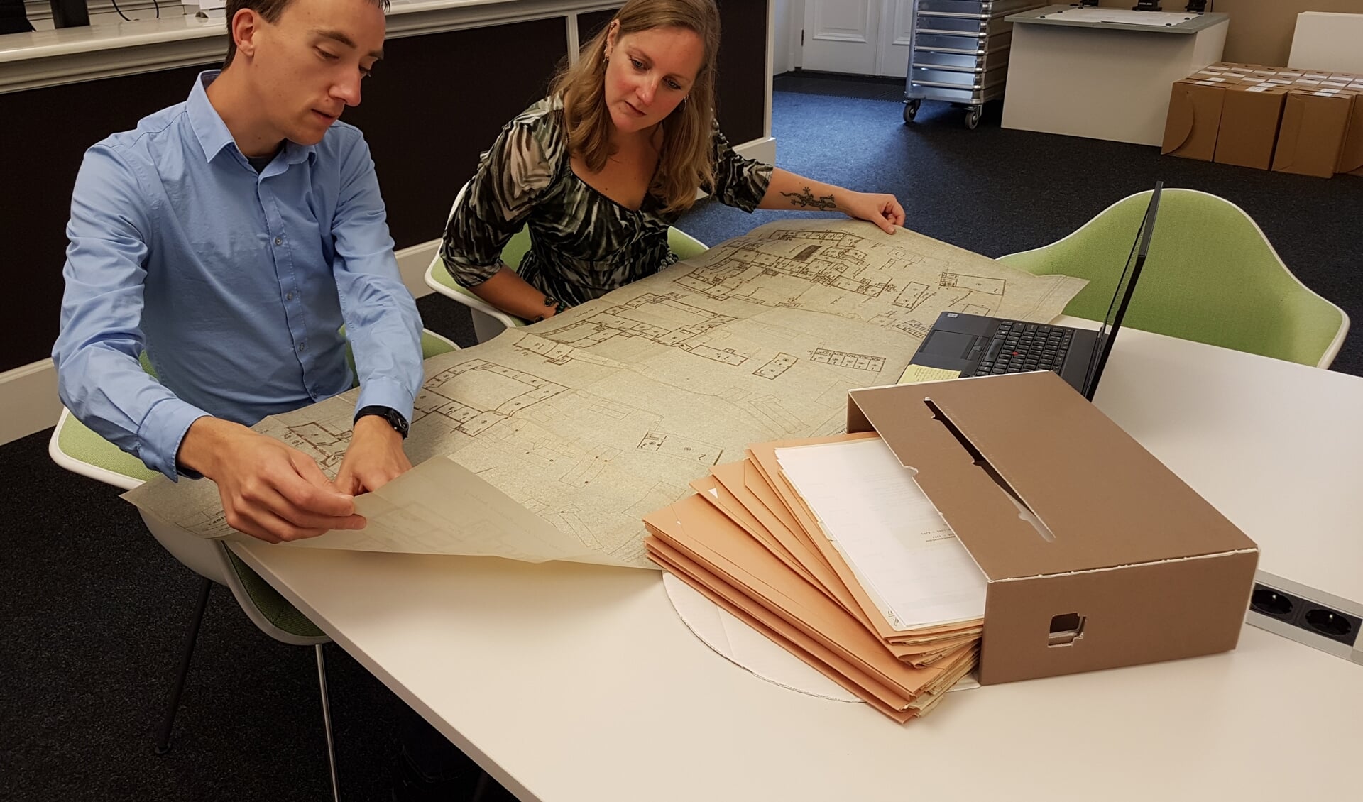 Onderzoeker Bart van Eekelen toont medewerker Dienstverlening Saskia van Bavel een plattegrond van het Markiezenhof die het West-Brabants Archief voor hem heeft gedigitaliseerd.