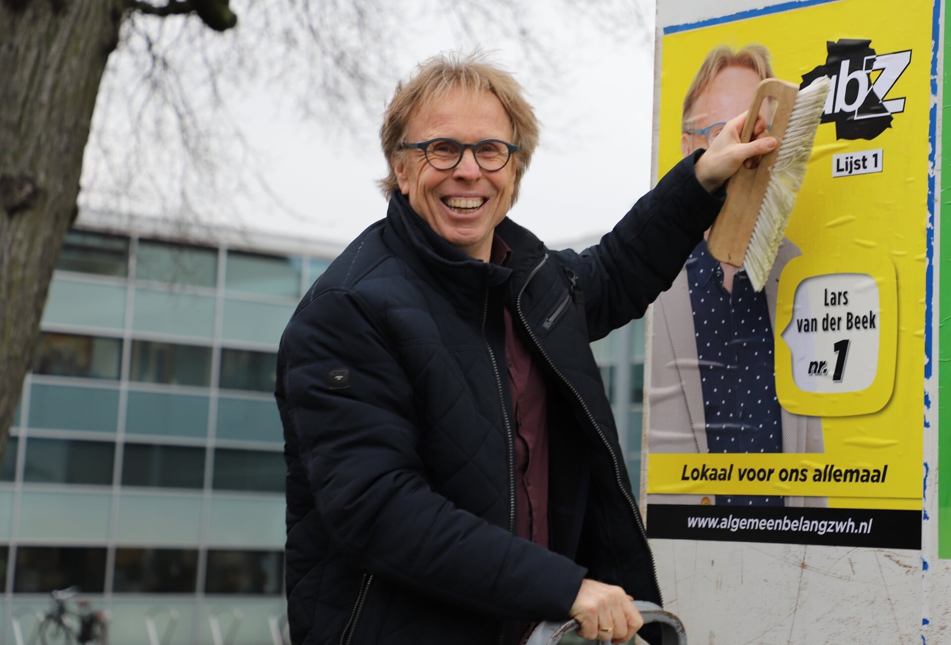 Lars van der Beek plakt eigenhandig de verkiezingsposter op het bord voor het gemeentehuis.
