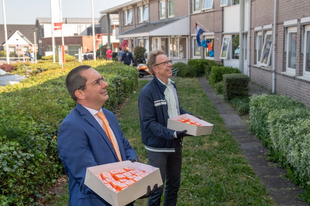 Burgemeester Adriaansen en wethouder Van der Beek delen op Koningsdag gebak uit.