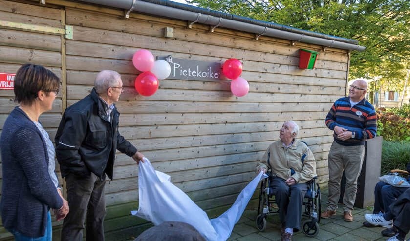 Piet van der Spank onthult vanuit zijn rolstoel het naambord van de houtbewerkingsruimte 'Pietekoike'.