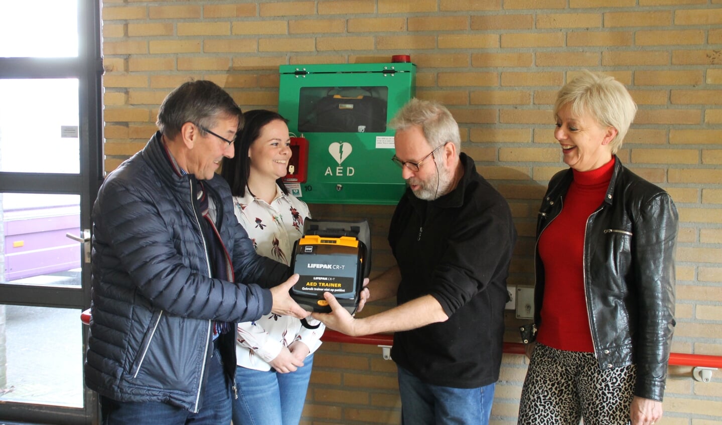 De hoofdrolspelers kijken naar een AED die Klaas Haan heeft meegenomen om het belang ervan te duiden.