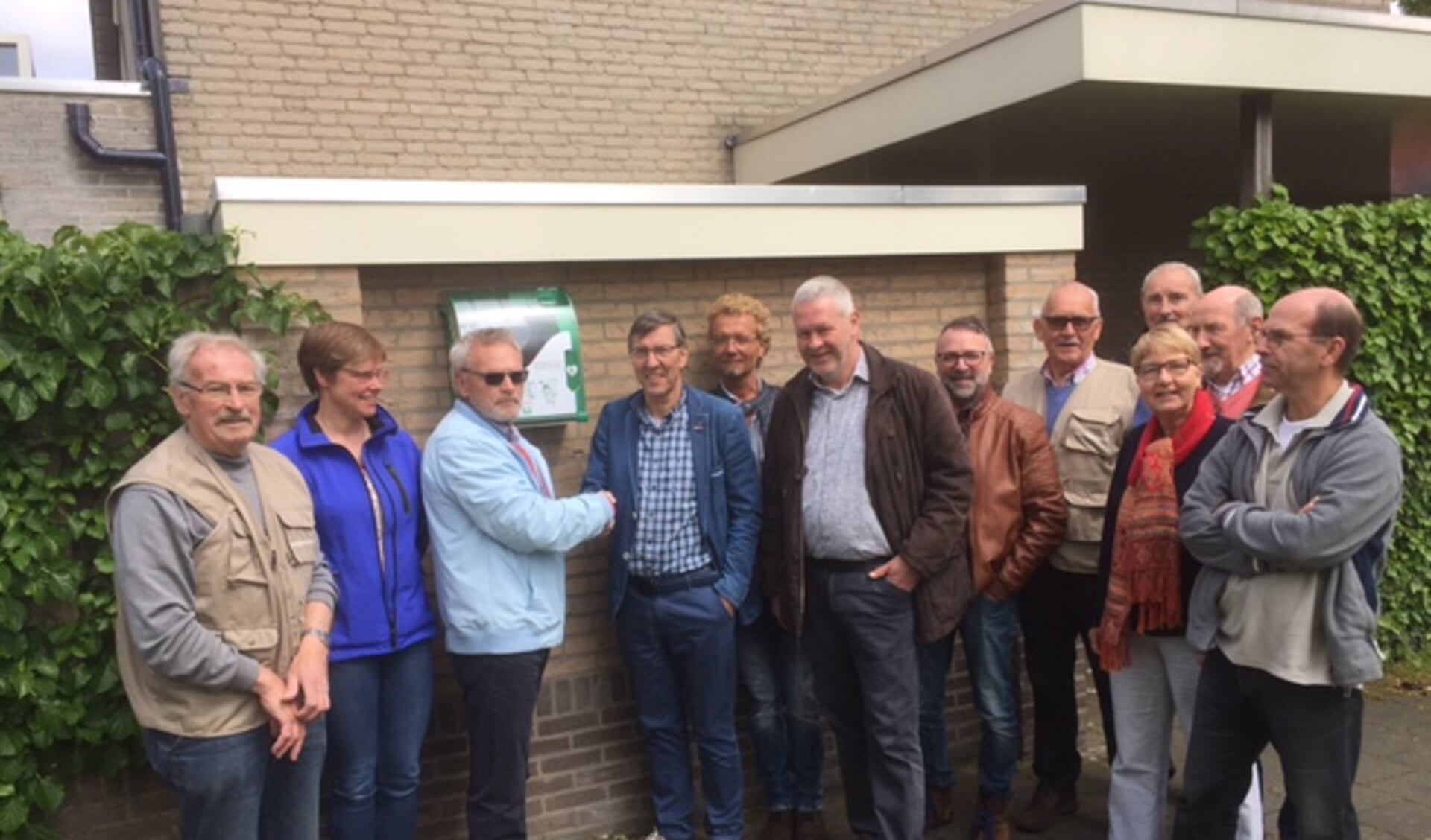 Diverse mensen uit de buurt die bij het project betrokken zijn waaronder de potentiële hulpverleners. Arie Dijkhuizen, voorzitter Wijkraad de Bunders, en Klaas Haan, Voorzitter Veghel HartSave, schudden elkaar de hand.