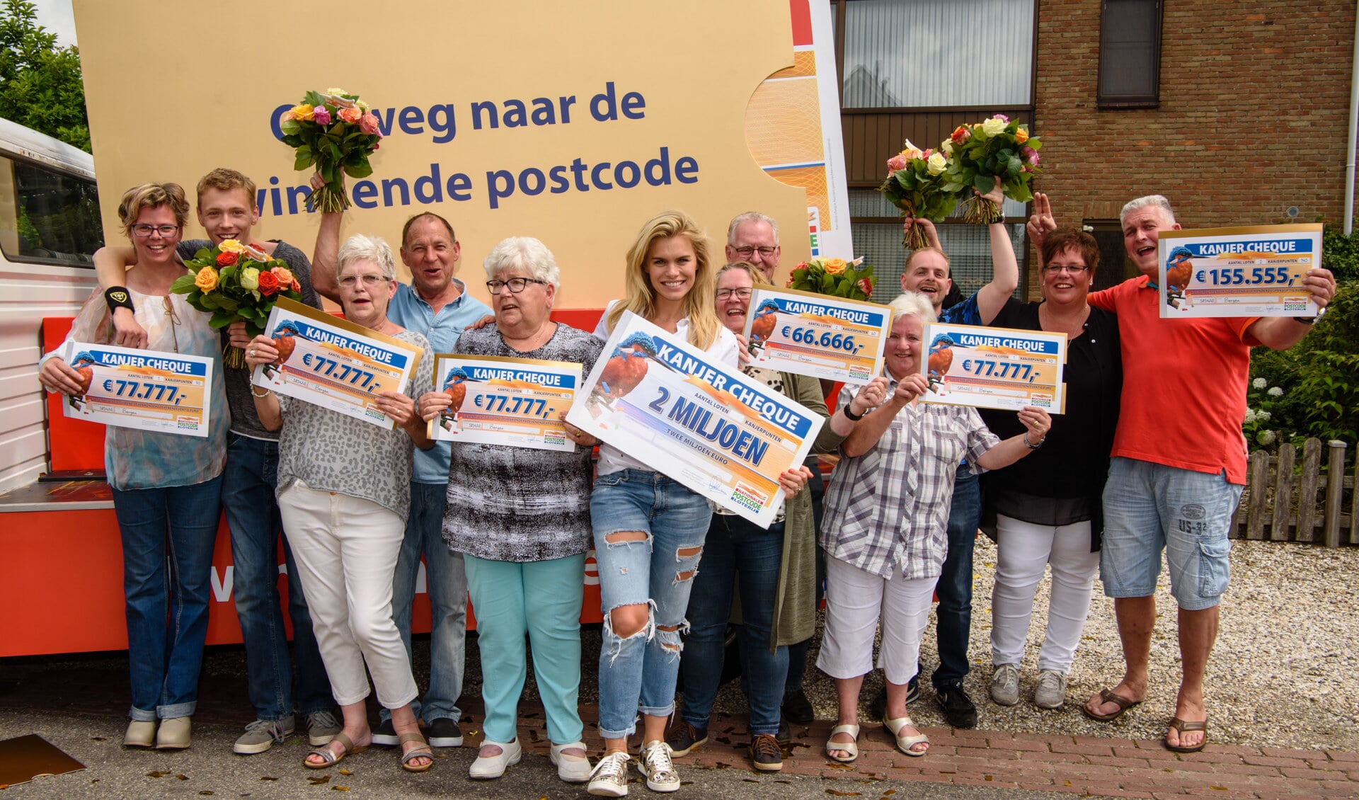 De blije winnaars van de grote prijzen van de Postcode Loterij  (PL) op een rijtje in Bergen met in het midden  PL-ambassadrice Nicolette. Foto: Roy Beusker Fotografie