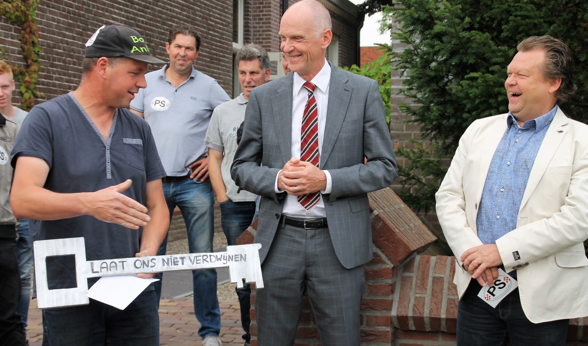 Boer Anton reikt burgemeester Fränzel de hand. Wethouder Eus Witlox kijkt lachend toe.