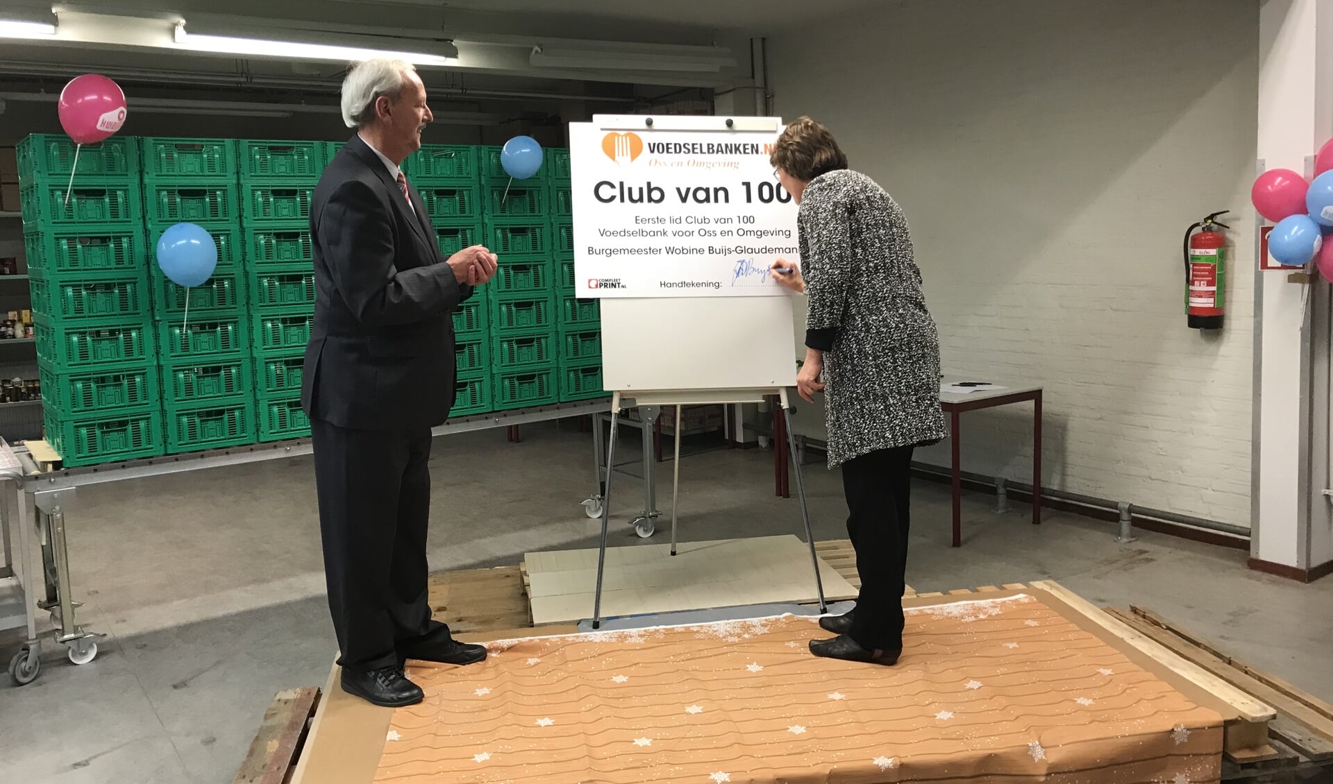 Burgemeester Wobine Buijs van Oss tekent als eerste lid van de Club van 100 van de Voedselbank voor Oss en Omgeving haar overeenkomst. Links haar voorganger Herman Klitsie.  
