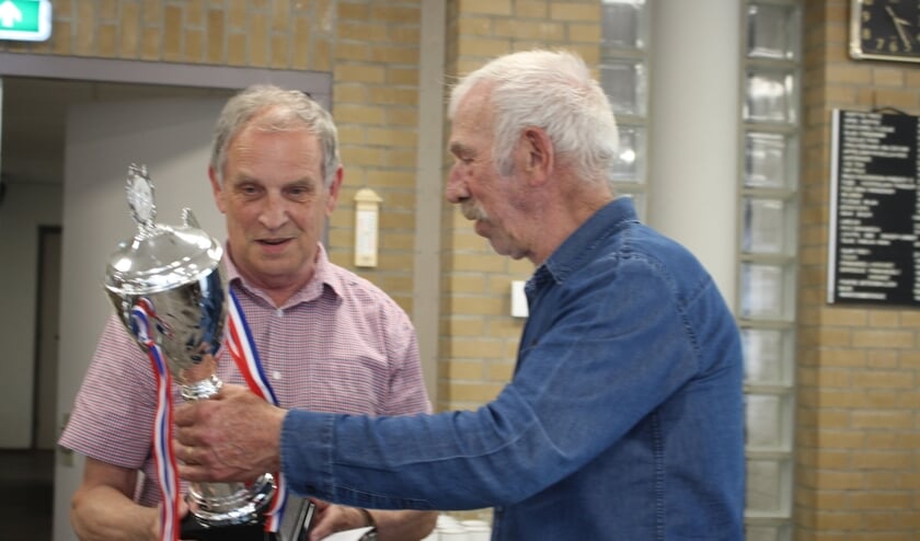 Joris Remmen neemt als teamleider van de biljartvereniging van KBO Wanroij de felicitaties en de wisselbeker in ontvangst uit handen van Christ de Vocht
