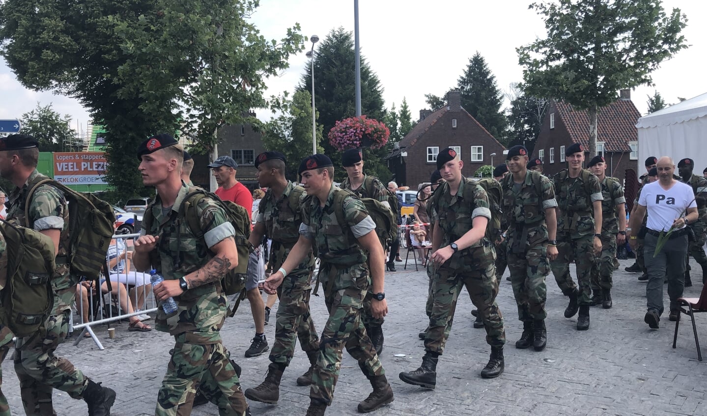 Militairen marcheren door het centrum van Mook, dat de wandelaars op weg naar de Via Gladiola in Nijmegen verwelkomt.