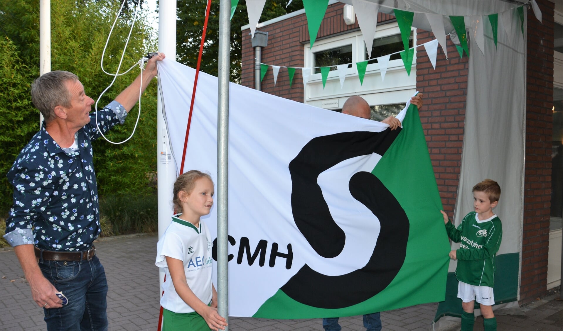 Erelid Bert van den Broek onthult de nieuwe vlag samen met de pupillen Lynn en Morris.