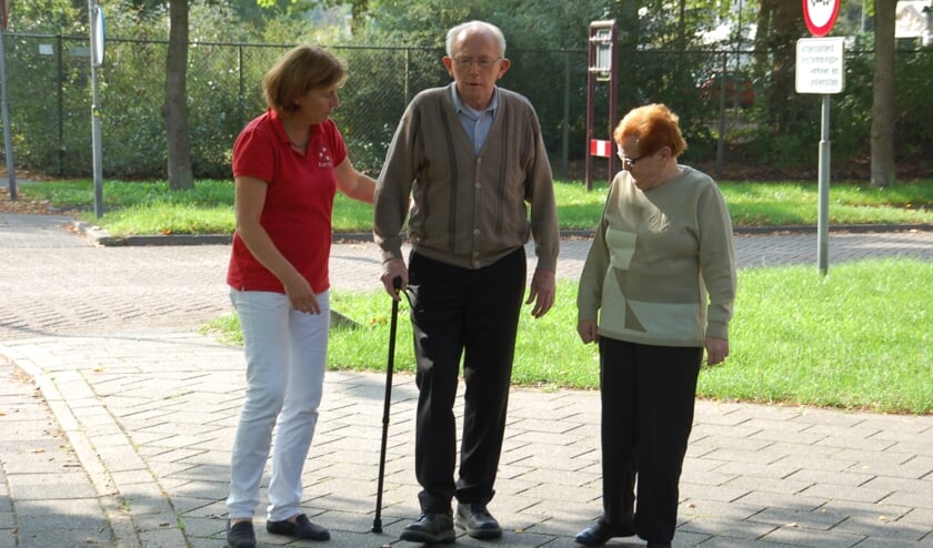 Marian op een archieffoto met een patiënt die uitleg krijgt over het lopen met een stok.