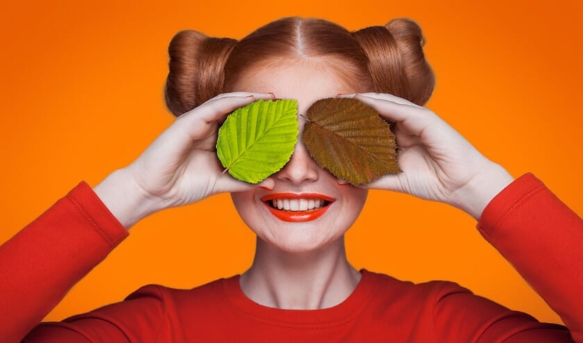 Young beautiful funny fashion model with orange slice on orange background. with orange makeup and hairstyle and freckles. holding orange between eyes with toothy smile.