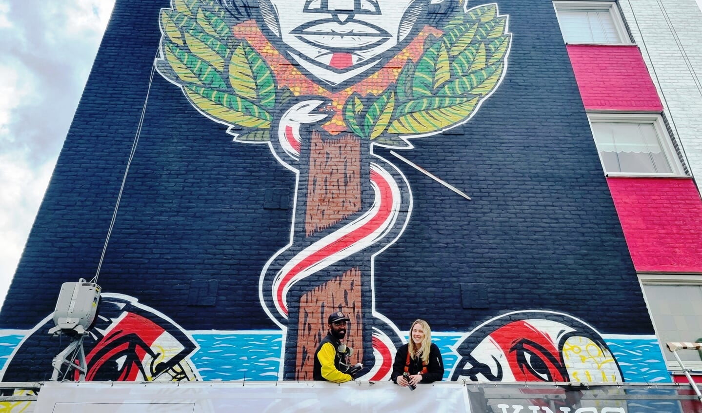 De Braziliaanse kunstenaar Pixote Mishu poseert samen met zijn assistente Bailey Birtchet bij de muurschildering op het flatgebouw in de wijk Boschveld.