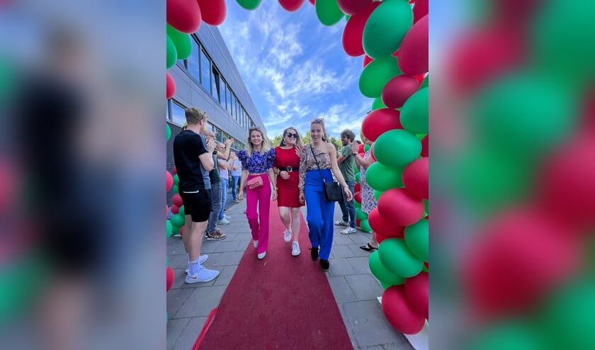 Geslaagden over de rode loper onder luid applaus van docenten en door een boog met rode/groene ballonnen op Metameer jenaplan Boxmeer.