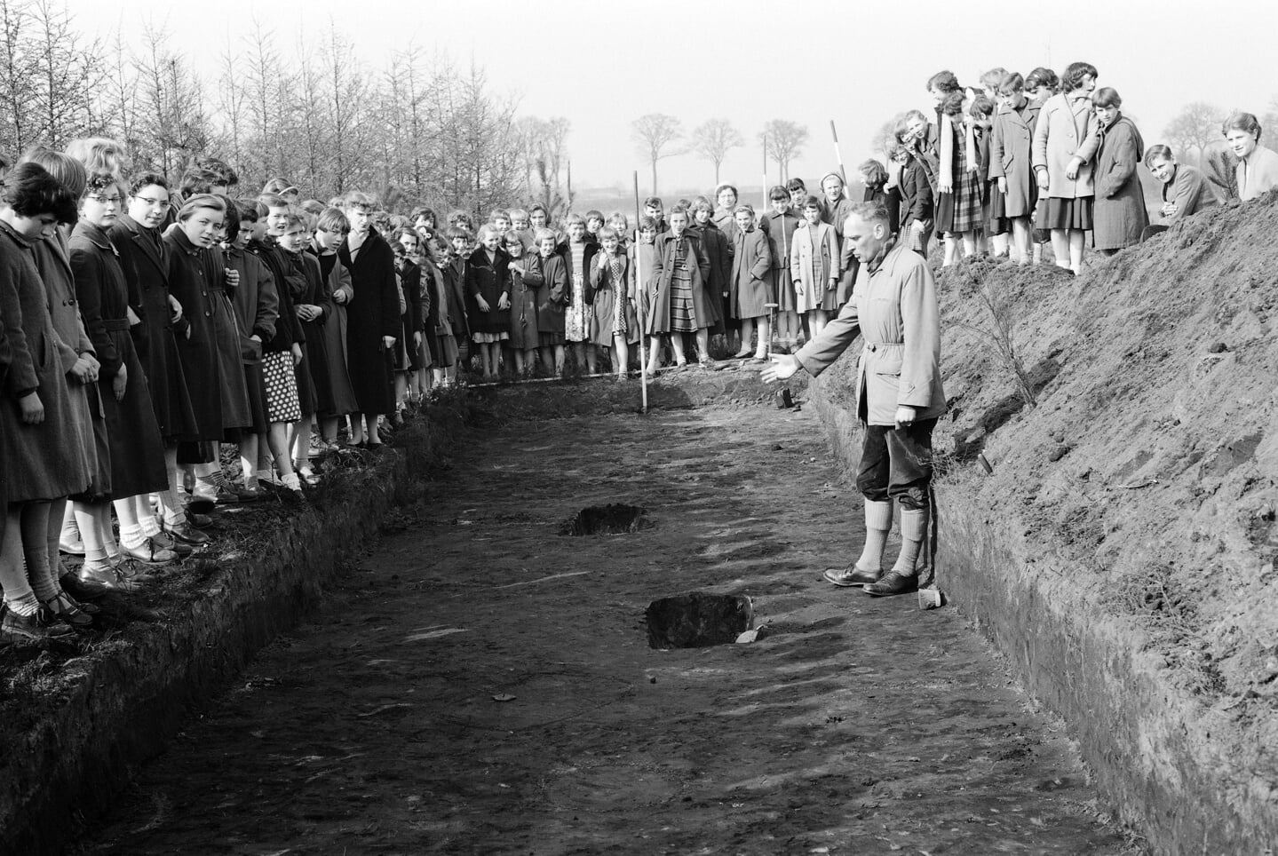 Al jarenlang graven archeologen in Oss op, zoals hier in 1956. Prof. Modderman, die aan de wieg staat van het onderzoek in Oss, geeft uitleg aan schoolkinderen.