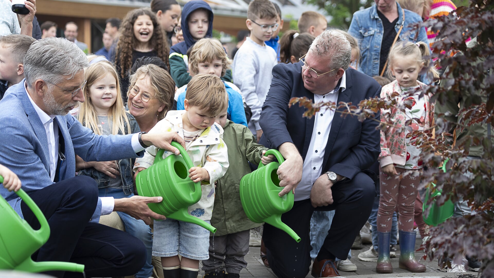 Voorzitter College van bestuur Verdi Paul Meessen en wethouder Johan van Gerwen geven samen met de kinderen water aan de boom die symbool staat voor De Wijzelaar.