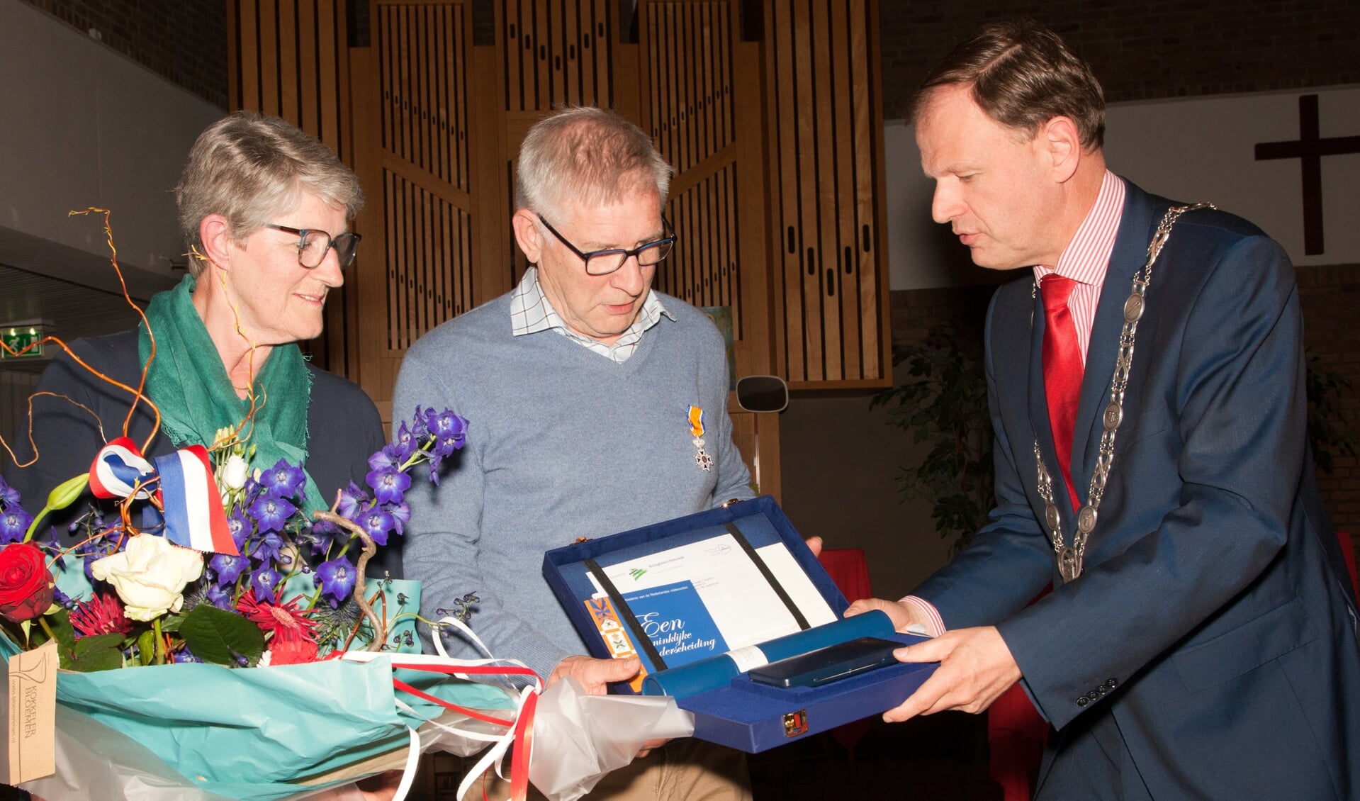 Onder toeziend oog van zijn echtgenote overhandigt burgemeester Van der Kamp de bij de onderscheiding behorende oorkonde aan Hans Rootert