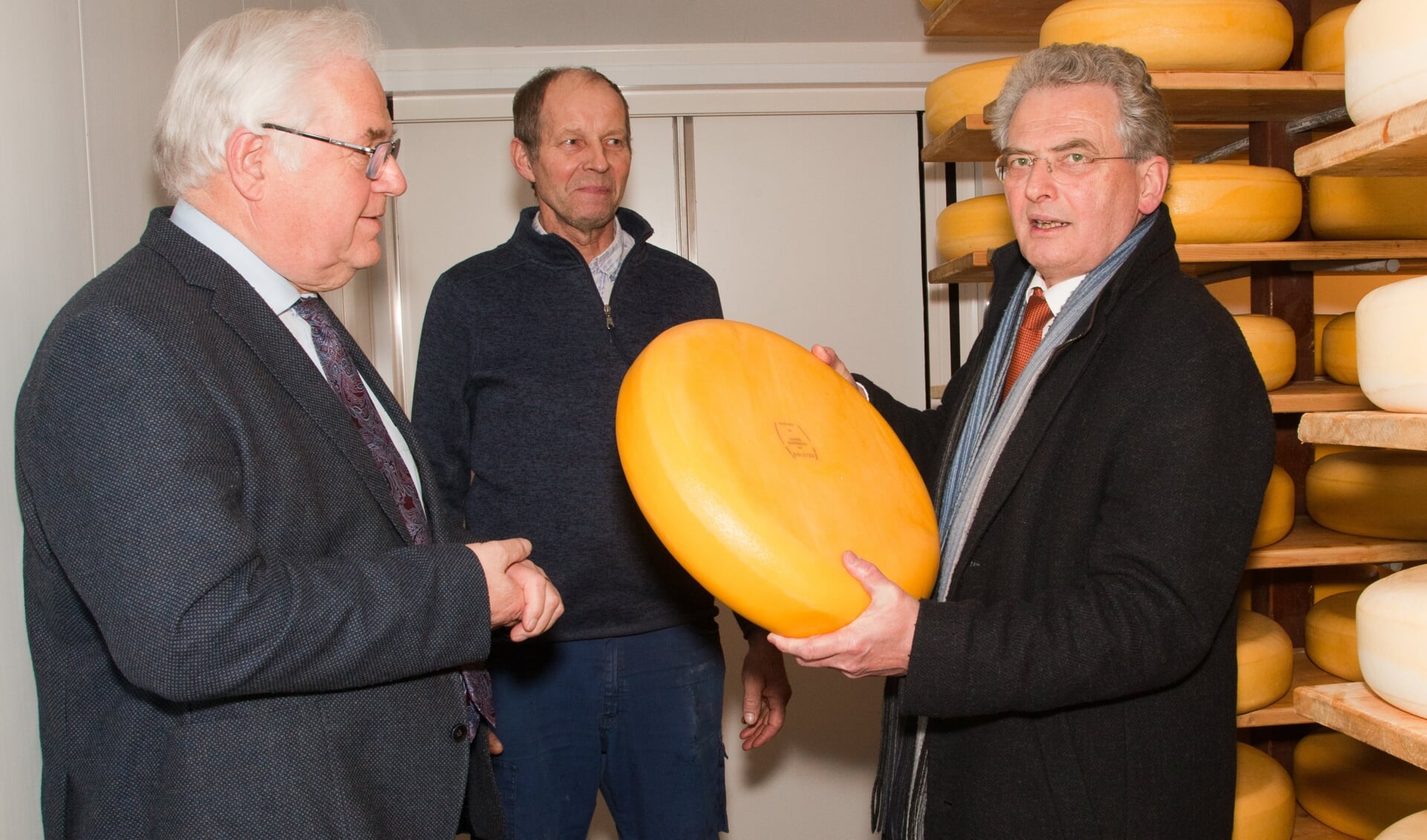 Raadslid Henk van der Smit en Wim Olieman kijken toe hoe de heer Bisschop het gewicht van de kaas inschat.