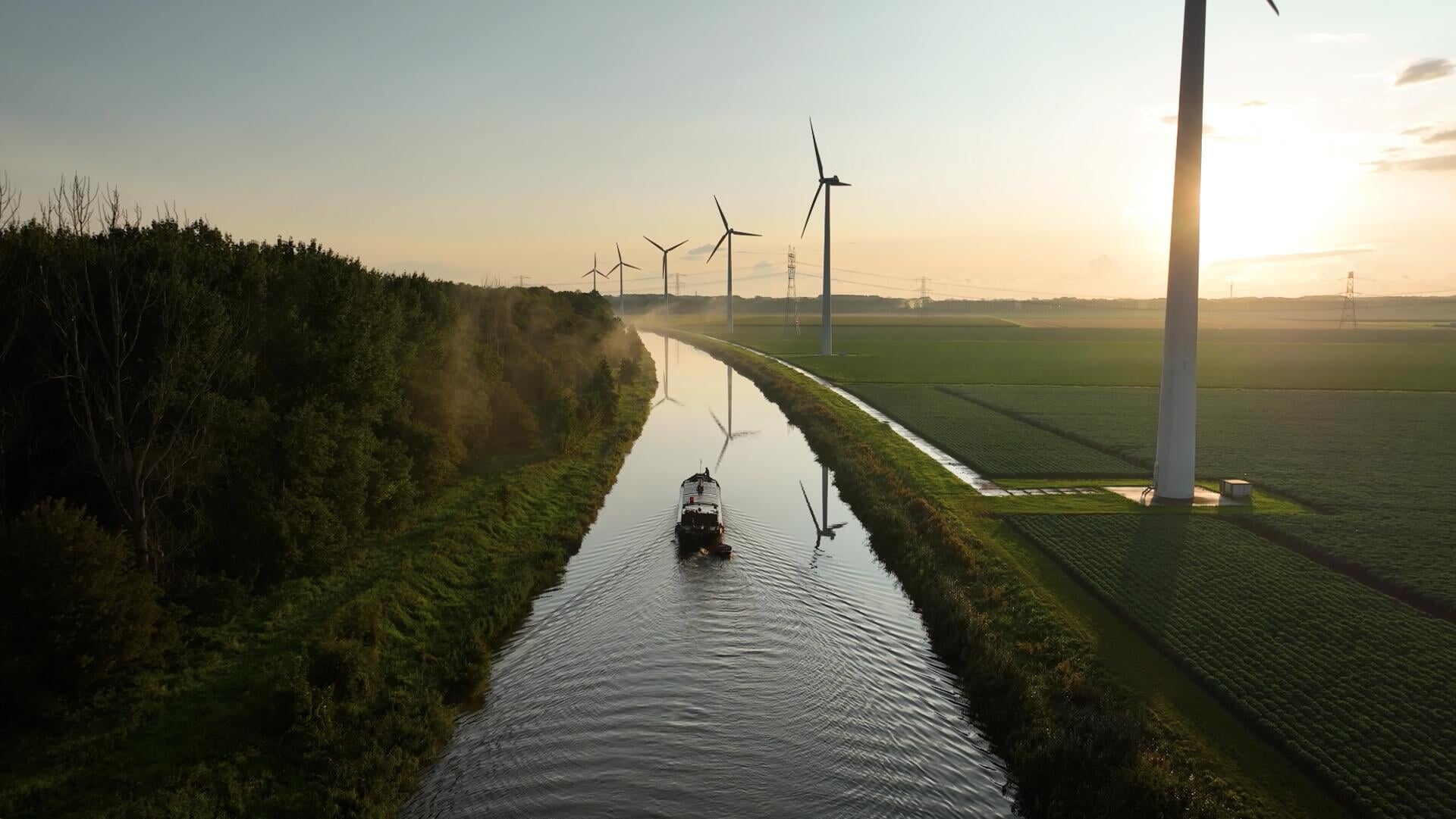 Een elektrische boot vaart langs een polder met windmolens.