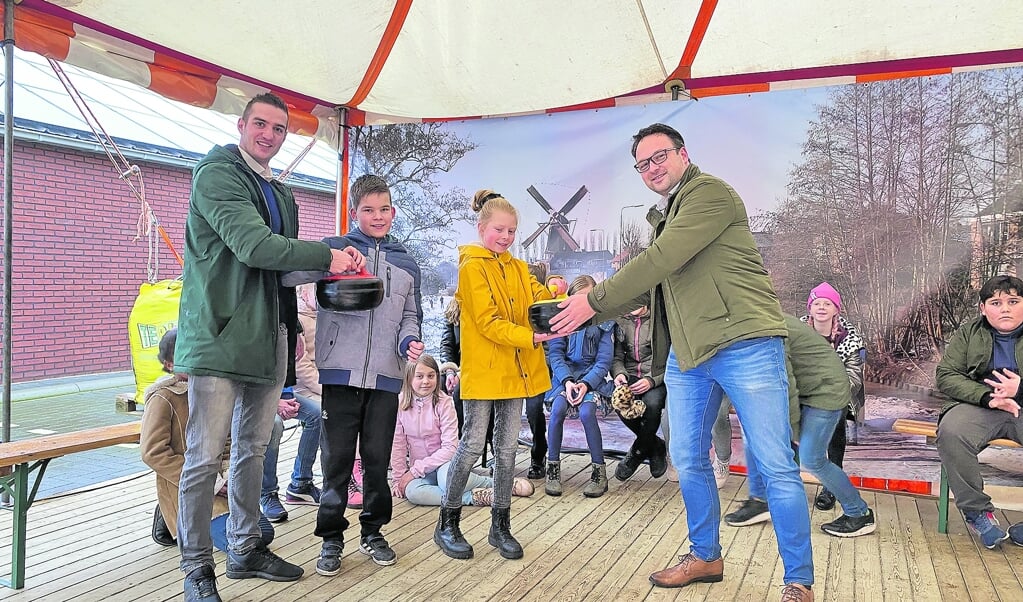 Merlijn van der Does van Veenbrink RVS (links) en Jaap-Jan Aarnoudse van Jumbo (rechts) overhandigen de curlingstenen officieel aan de kinderen van de Graaf Jan van Montfoort school.