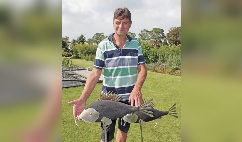 <p pstyle="BODY">Joop bij zijn kunstwerk in de tuin. Twee karpers gevormd met onder andere messen, kaasschaaf en uiteinden van bestek.</p>