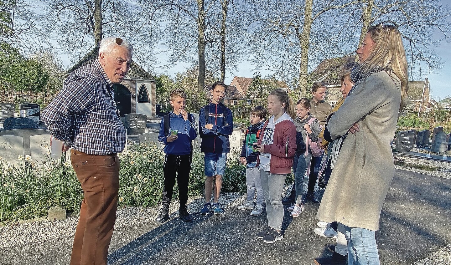 Hans Elzas geeft uitleg aan een groepje kinderen bij de oorlogsgraven.