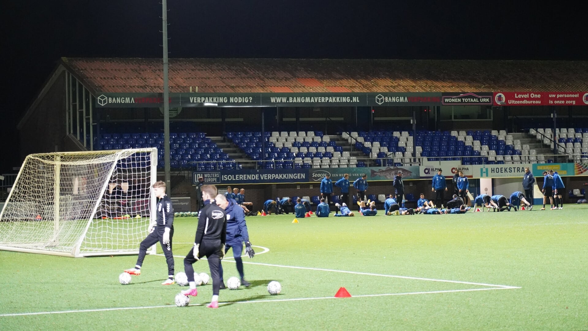De keepers werken onder leiding van trainer Peter de Boer een aparte training af, terwijl op de achtergrond de veldspelers bezig zijn met de warming-up.
