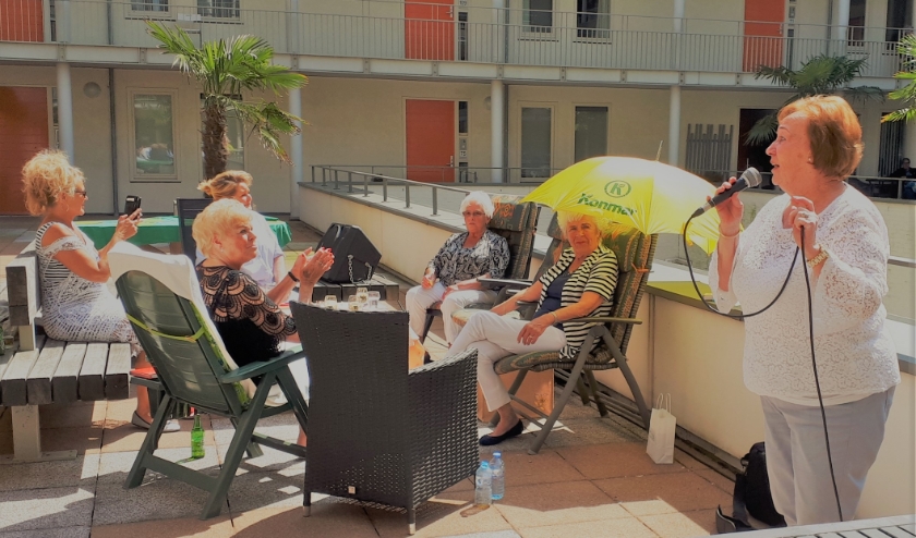 Op de foto is Annie aan het zingen, mevrouw Kurvers onder de gele parasol werd 81 jaar die dag. De stemming zat er goed in tijdens de Balkonbingo...