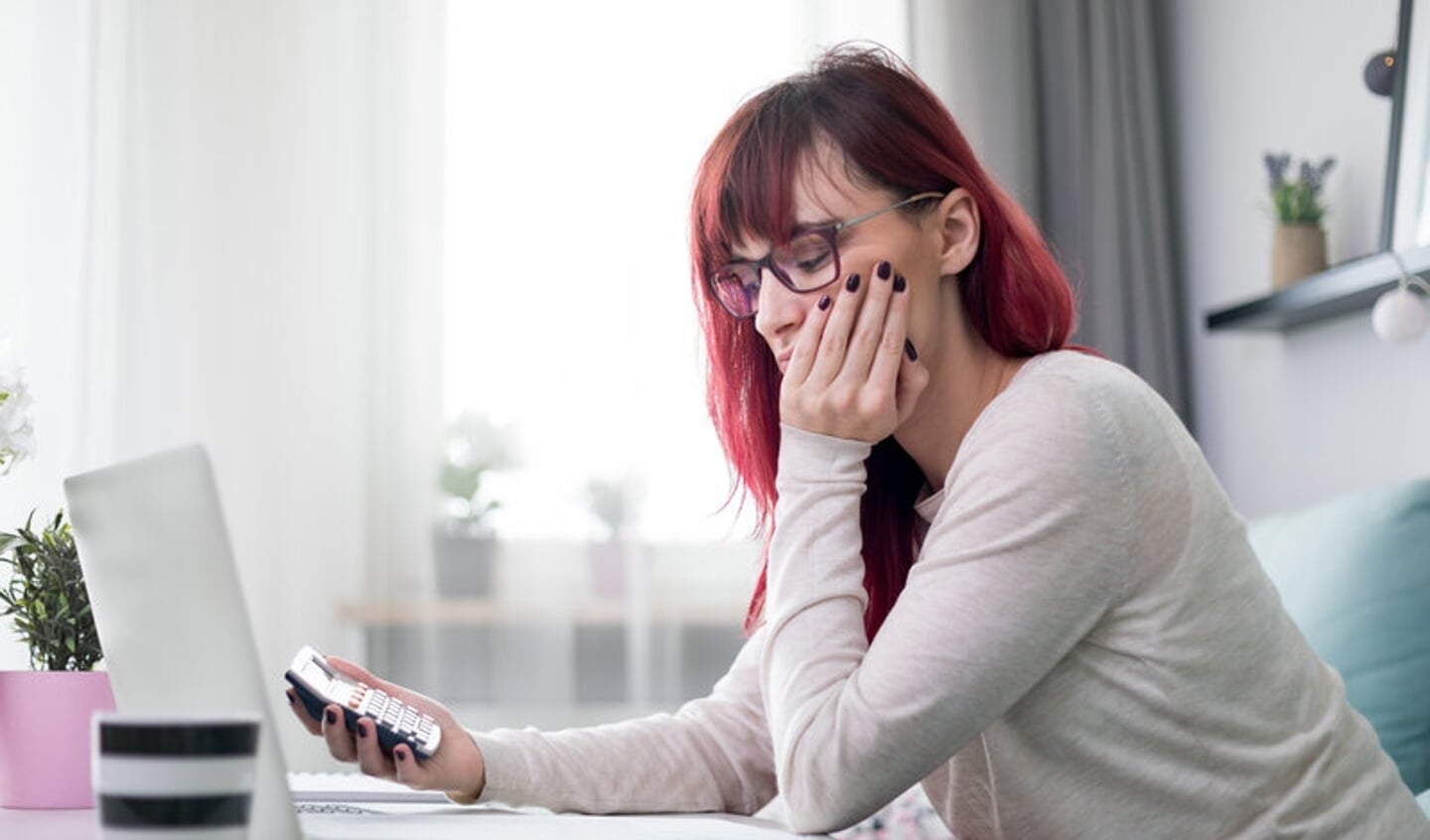 Worried woman at home checking financial documents using calculator and laptop