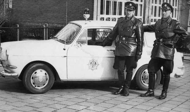 <p>De hoofdagenten Sollie en Punt bij hun surveillanceauto</p>