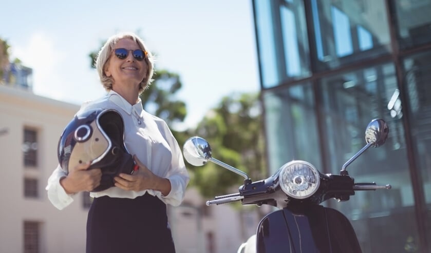 Smiling businesswoman holding helmet while standing by motor scooter