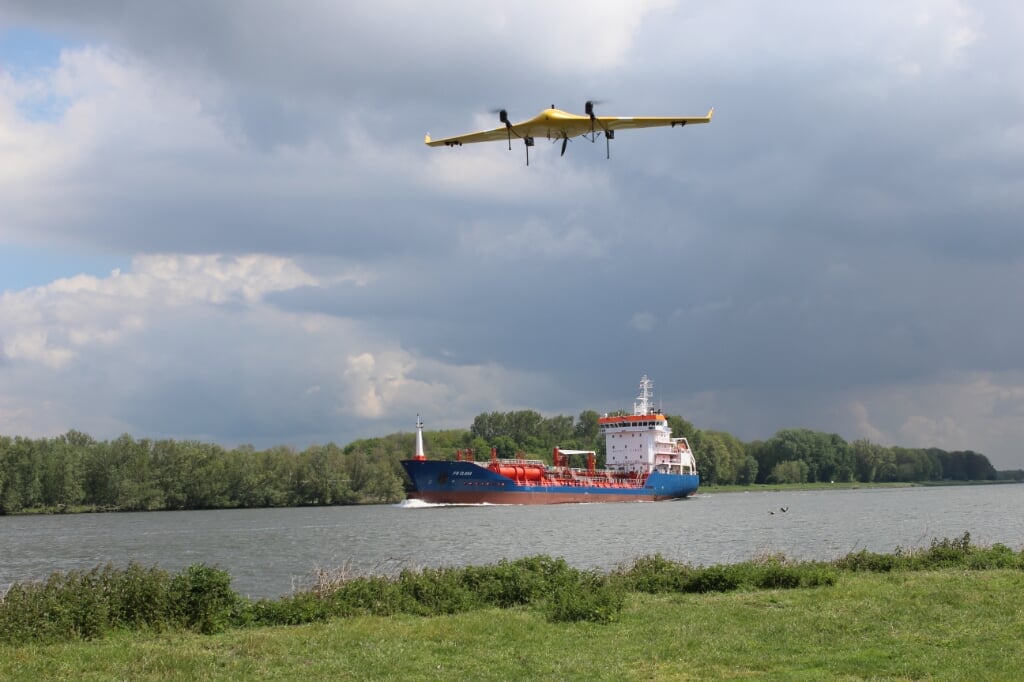 De drone kruist een rivier met scheepvaartverkeer. 