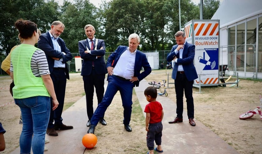 Staatssecretaris Eric van der Burg spreekt met een vrijwilliger (op de rug gezien) terwijl hij voetbalt met een van de kinderen van de crisisnoodopvang.