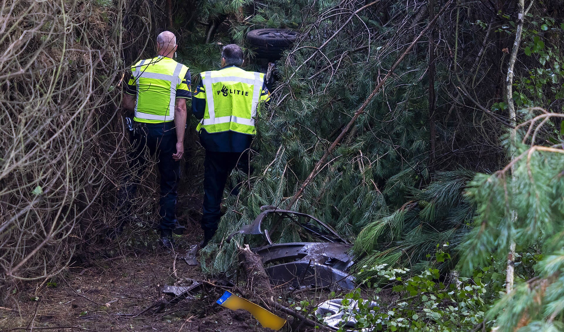 De politie bij het wrak, dat diep in de bosschage belandde na de botsing.