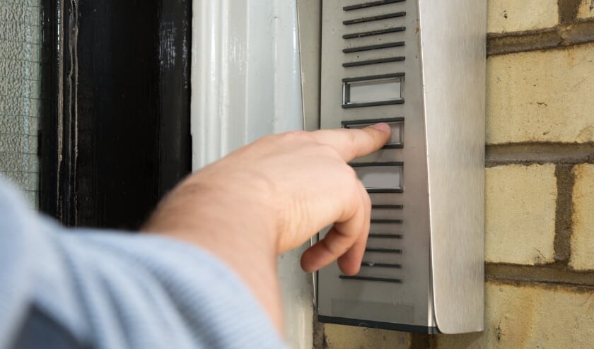 Close up view of the hand of a man ringing an intercom to gain access to an apartment building or business premises, wall-mounted on brickwork