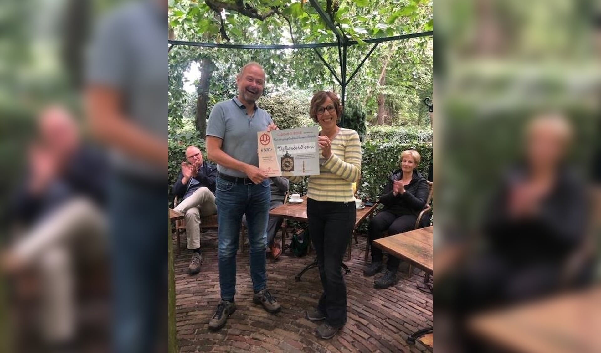 Burgemeester Patrick Welman, tevens voorzitter van de Oudheidkamer Twente, neemt een cheque in ontvangst van Harriet Tomassen van Crematoria Twente. 