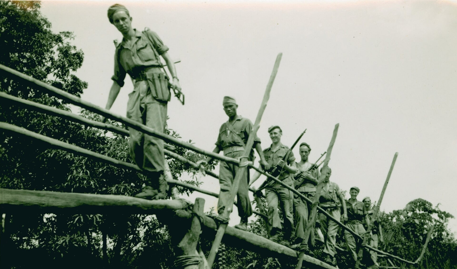 Nederlandse militairen passeren een houten loopbrug ergens in het toenmalige Nederlands-Indië.