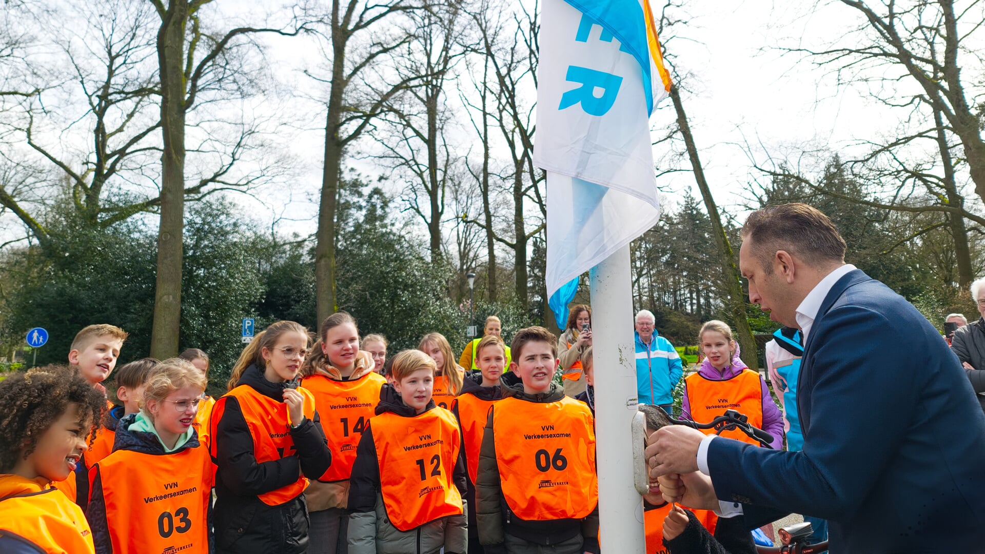 Met de hulp van een leerlinge hijst wethouder René de Koff de vlag als startsein voor het verkeersexamen van VVN Rijssen-Holten.